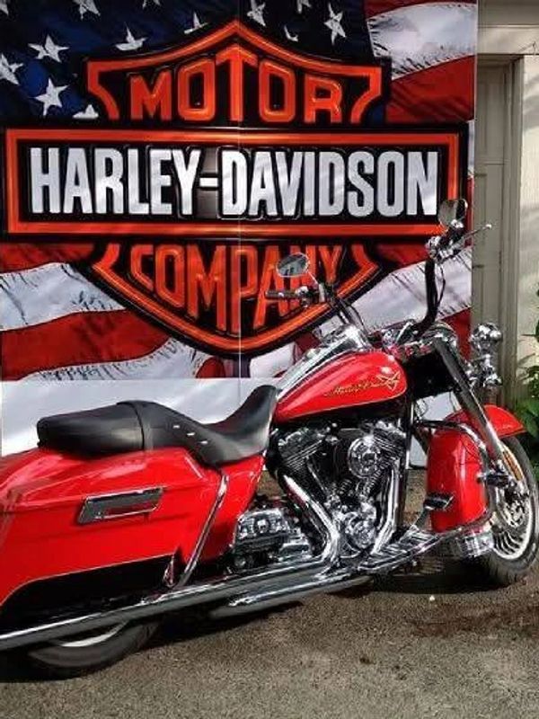 Red Harley-Davidson motorcycle parked in front of a patriotic American flag backdrop.
