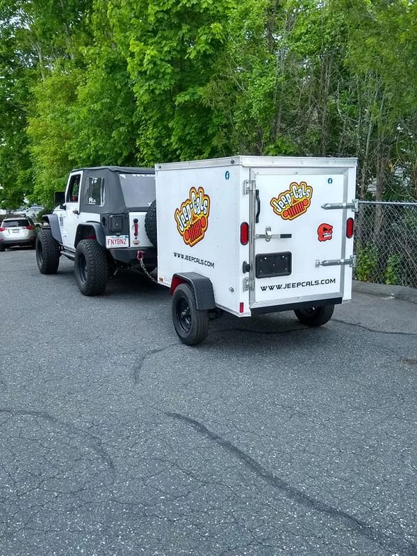 White Jeep towing a small branded trailer on a street.