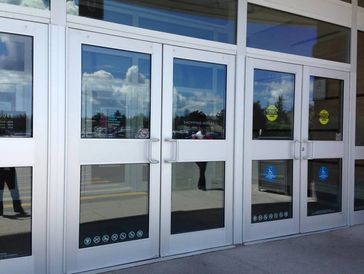 Glass entrance doors of a shopping center with visible signs and reflections.