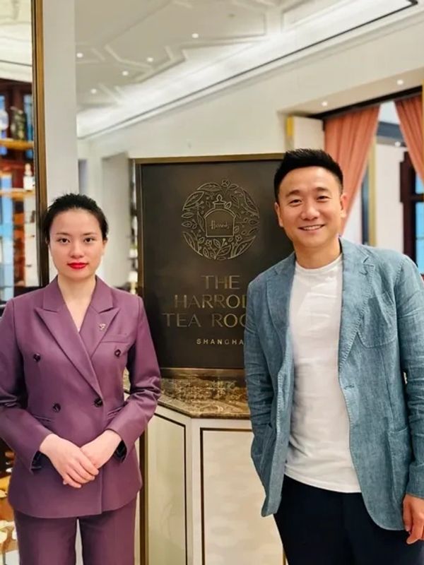 Two people standing in front of The Harrods Tea Room sign in Shanghai.