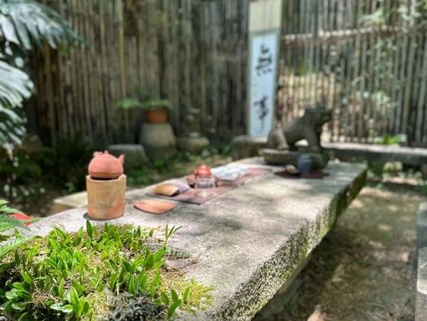 Outdoor stone table set with tea utensils in a serene garden.