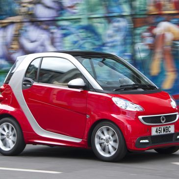 Red Smart car driving past a colorful graffiti wall.