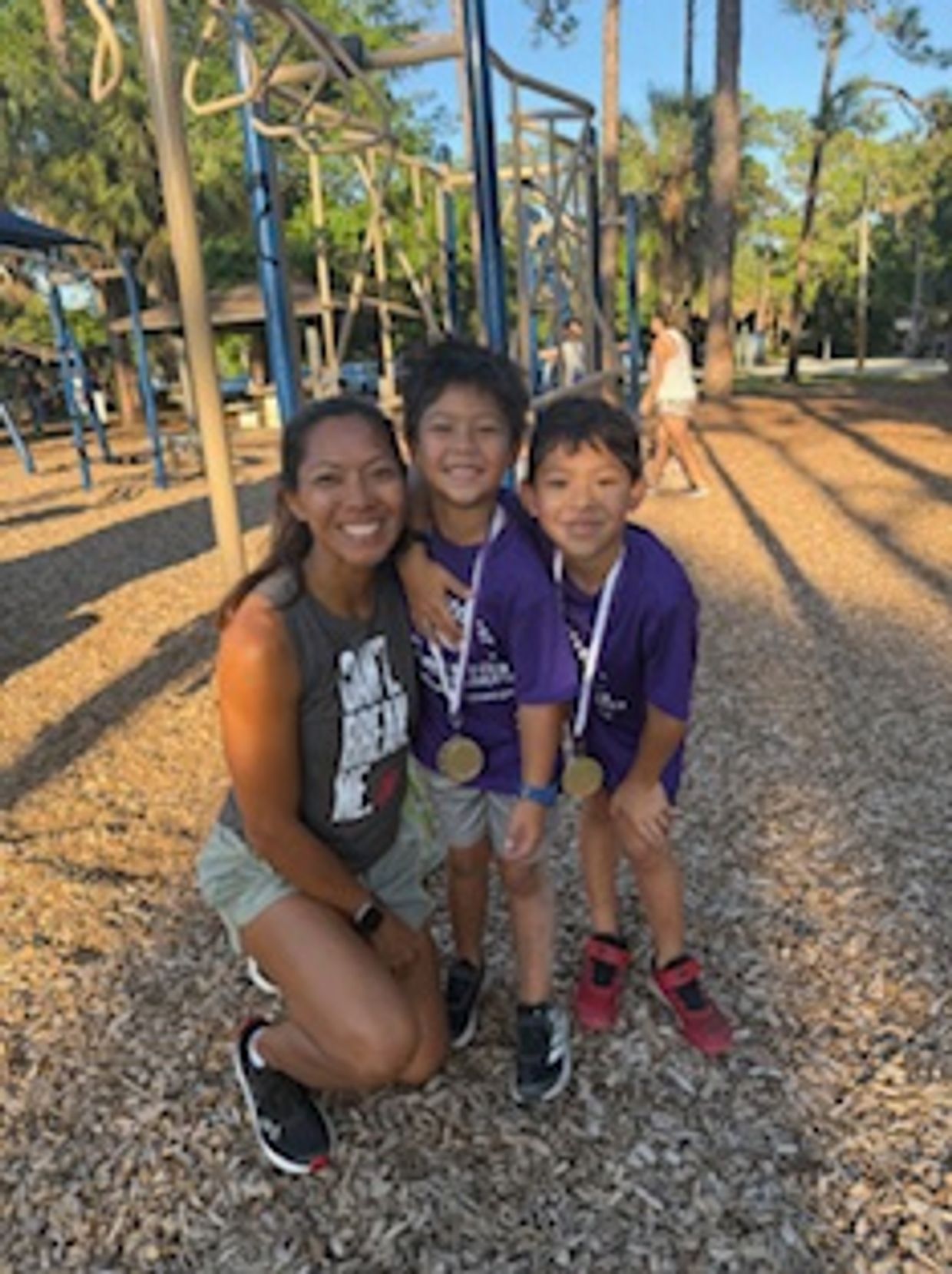A woman and two boys with medals at a playground, smiling happily.