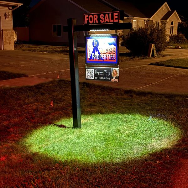 Illuminated 'For Sale' sign on a lawn at night in a suburb.