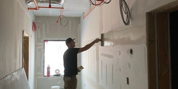 Worker smoothing drywall in construction site.