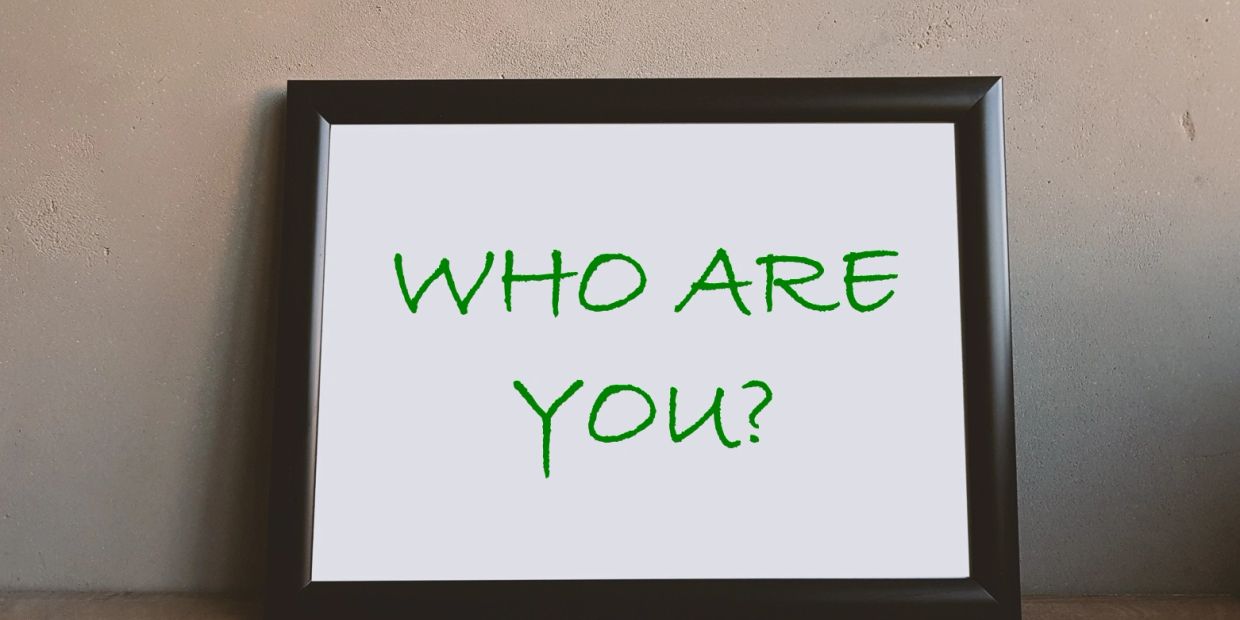Framed sign on a wall reads 'WHO ARE YOU?' in green text.