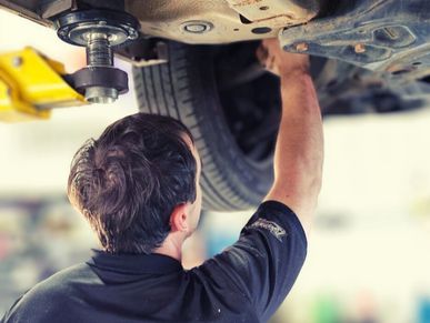 Mechanic checking ball joints and suspension parts on a lifted vehicle