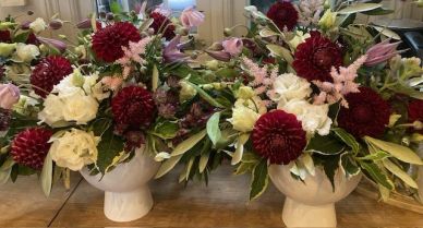 Two floral arrangements with red, white, and purple flowers in beige vases.