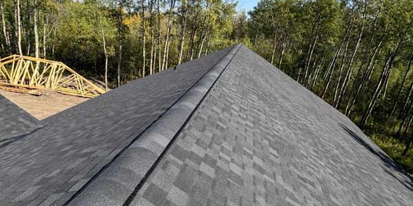 Newly shingled roof on a house under construction in a wooded area.