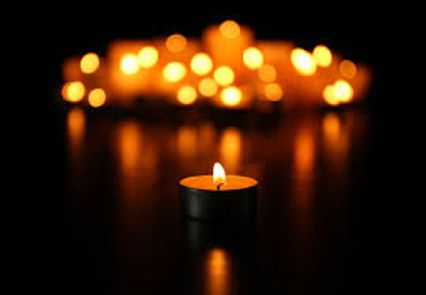 Image of tea light candle in foreground, with dark around and other blurred candles in background.