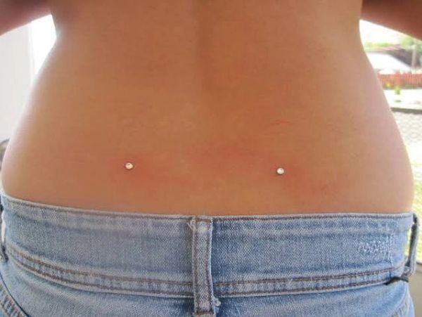 Lower back dermal piercings above jeans.