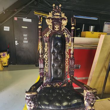Black and gold crocodile-textured throne with ornate wood carving displayed in a backstage venue area for event rental or celebrity use.