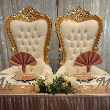White and gold tufted thrones staged for wedding head table with blush decor and “Mr & Mrs” nameplates.