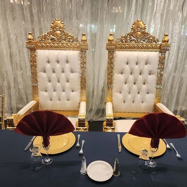 Square white and gold tufted thrones featured behind a banquet table setup for a formal or wedding reception.