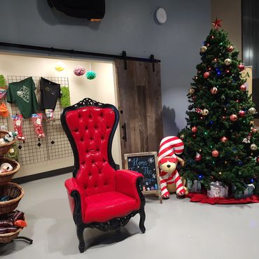 Red tufted throne with black frame beside decorated tree for a Christmas-themed event or photo station.