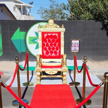 Red and gold throne placed in front of giant Christmas tree at outdoor event for public photo opportunities.