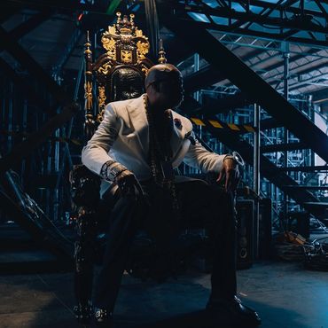Dark wood and gold throne with high backrest and crest detailing used on stage for VIP talent during a backstage promotional shoot.