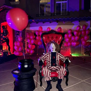 Red and black throne staged outdoors with clown figure and red balloons for a spooky Halloween photo setup.