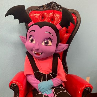 Purple cartoon mascot seated on red tufted throne with black frame for kids' party or entertainment event.