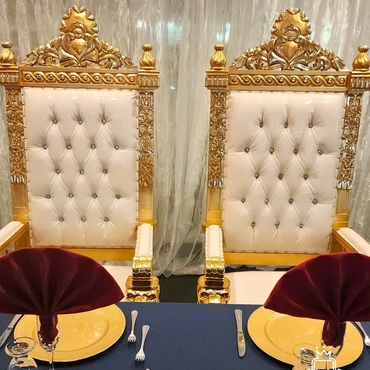 Pair of white tufted square thrones with gold frames set for formal dining at a banquet or wedding event.