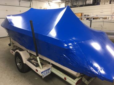 Boat covered with blue shrink wrap on trailer in garage.