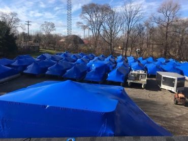 Rows of blue tarp-covered boats in an outdoor lot.