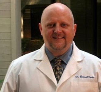 A smiling man in a white lab coat and tie.