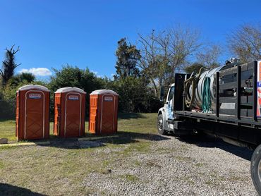Three orange portable toilets beside a service truck on a sunny day.