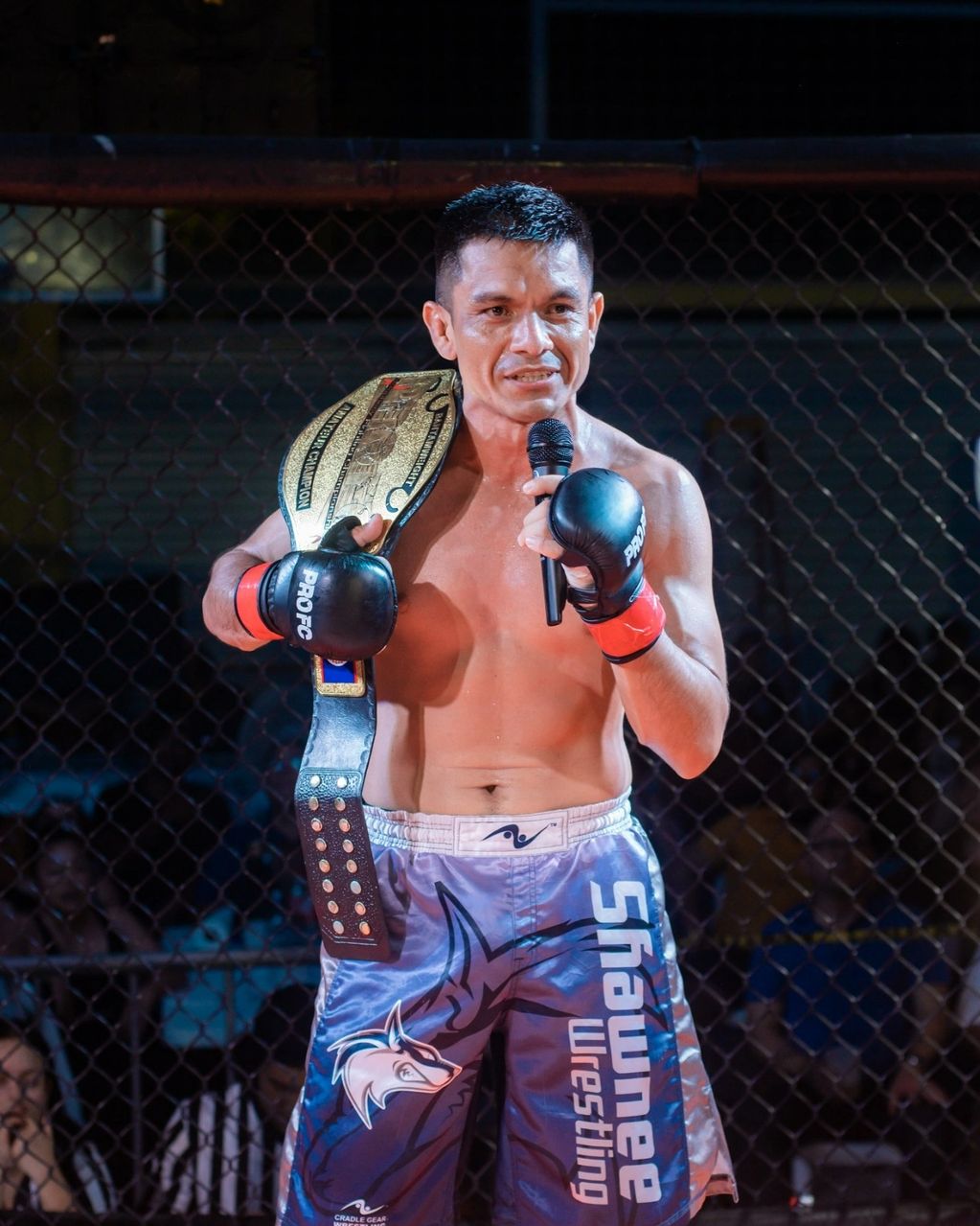 MMA fighter with championship belt speaking into microphone inside the cage.