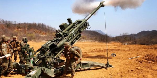 Soldiers operate a large artillery gun firing in a barren landscape.