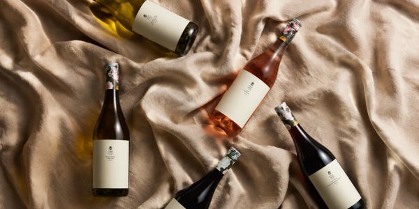 Five wine bottles with blank labels on beige fabric.