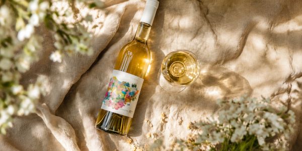 A bottle of white wine and a glass on a beige cloth with flowers.