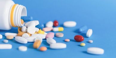 Various colored pills spilled from a white bottle on a blue surface.