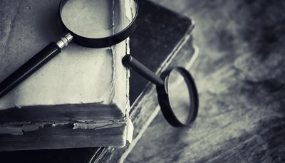 Magnifying glasses rest on old, worn books, evoking a vintage study atmosphere.