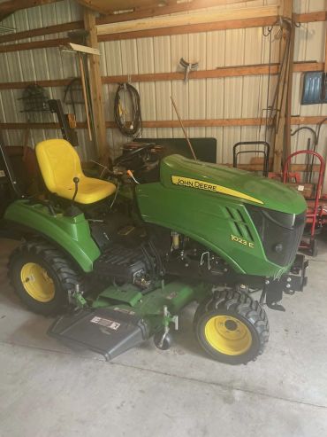 John Deere 1023E compact tractor with yellow seat in a shed.