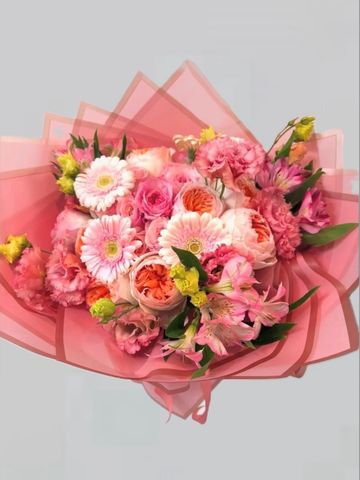 A vibrant bouquet of pink and peach flowers wrapped in soft pink paper.