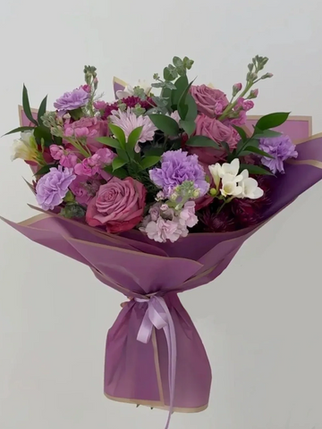 Elegant bouquet of purple and pink flowers wrapped in mauve paper with a ribbon.