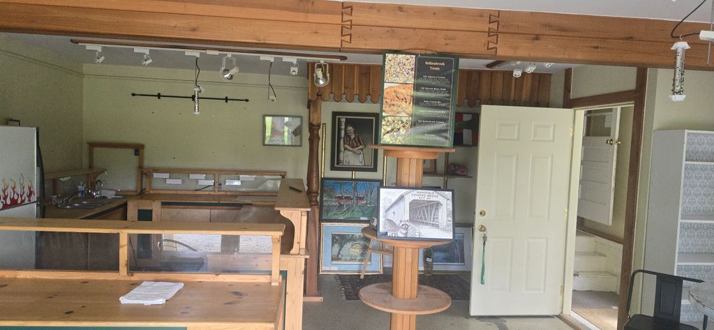 Interior of a rustic wooden shop with paintings and a display stand.
