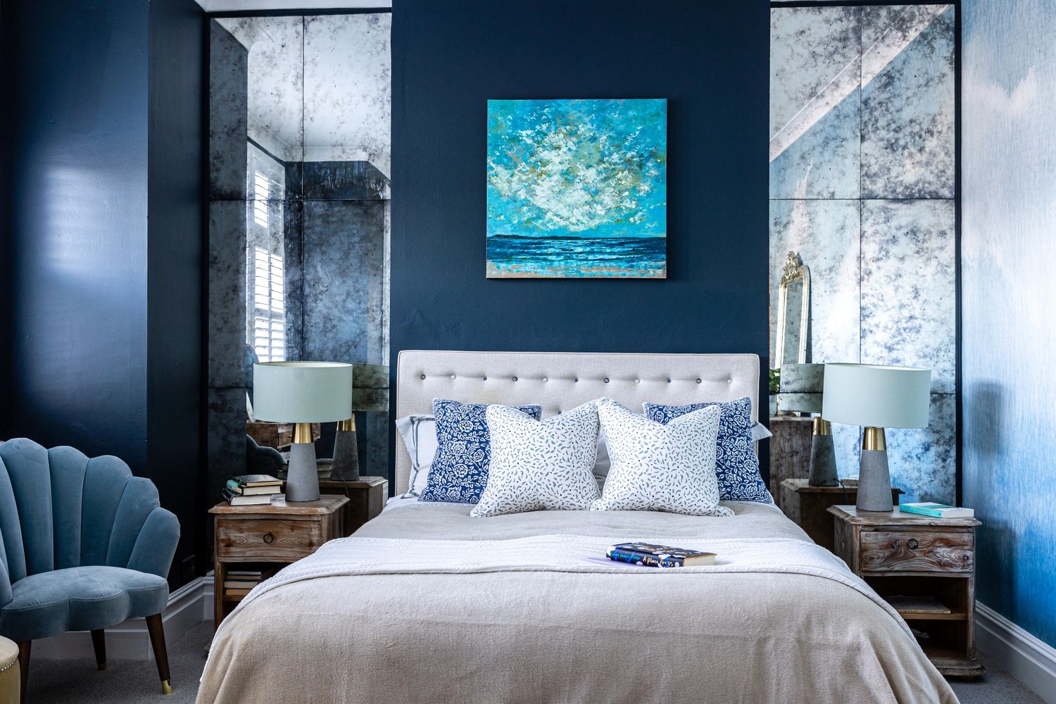 Master bedroom, dark blue walls, upholstered headboard, luxurious cushions, art deco velvet chair