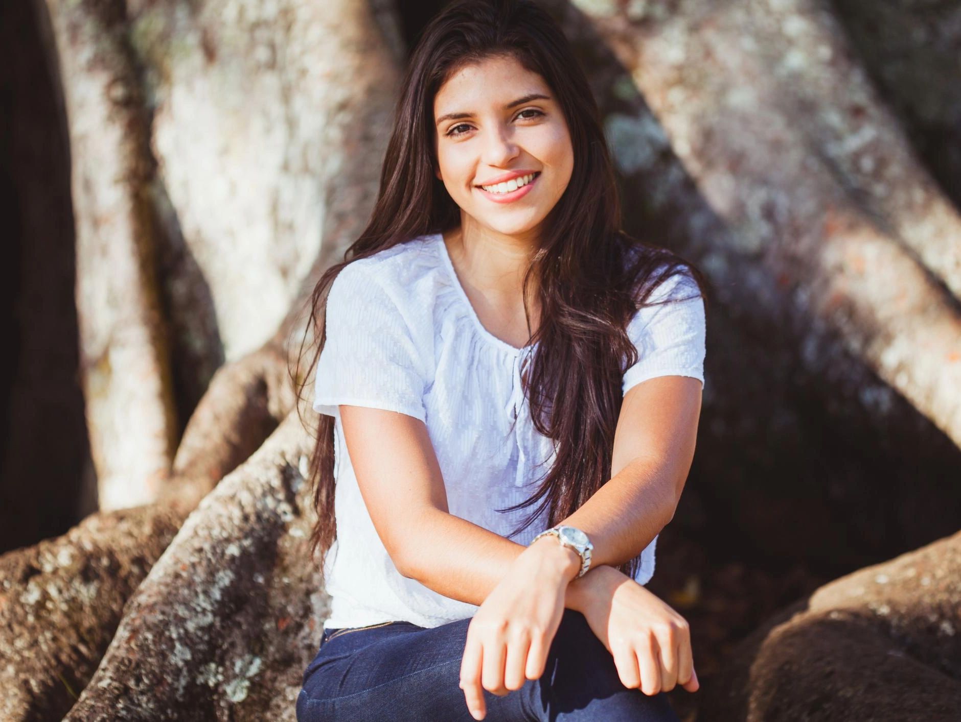 Young woman smiling outdoors near a tree.