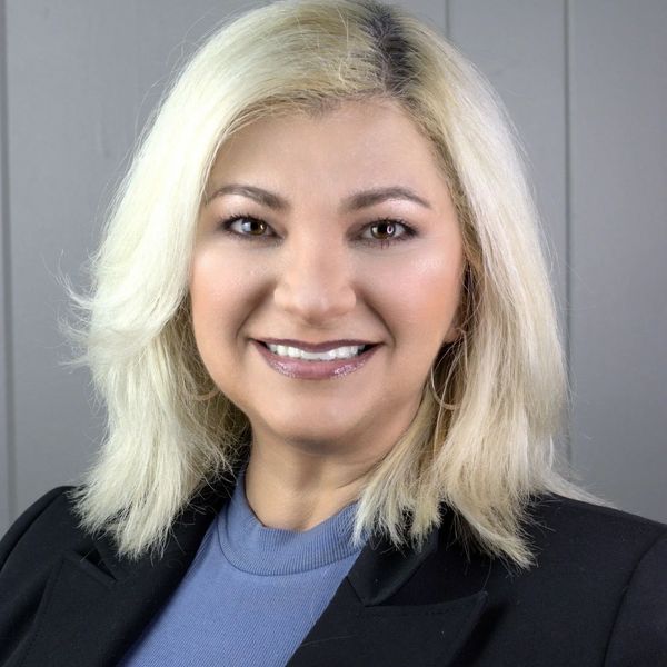 Smiling woman with blonde hair wearing a black blazer and blue top.