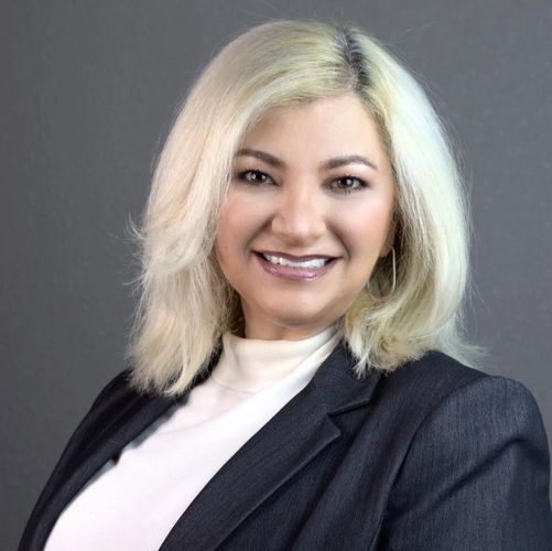 Professional woman with blonde hair smiling, wearing a black blazer and white top.