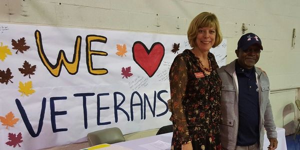 Two people standing by a 'We Love Veterans' sign at an indoor event.