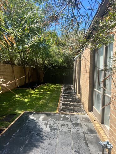A sunny backyard with a grassy lawn, stone pathway, and stairs leading to a gate.