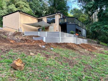 Modern house with large windows surrounded by greenery on a sloped hill.