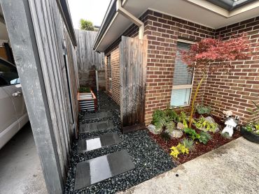 Neat backyard pathway with stepping stones, gravel, and plants beside a brick house.
