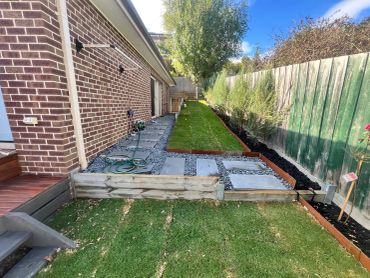 A backyard with a brick house, stone pathway, and green lawn.
