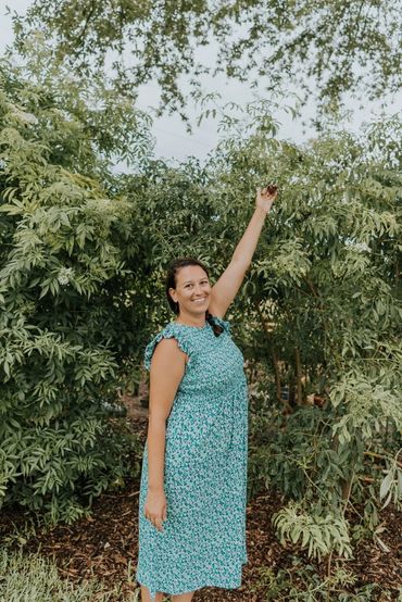 Smiling woman in a blue dress reaching up to pick berries from a tree.