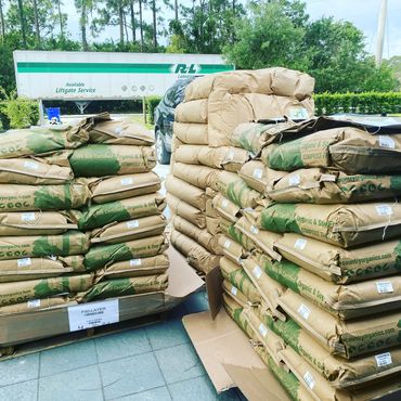Stacks of organic compost bags on pallets outdoors near a truck and car.