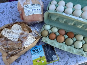 Farm-fresh eggs, bread, and poultry from Charmed Life Farm displayed on a table.